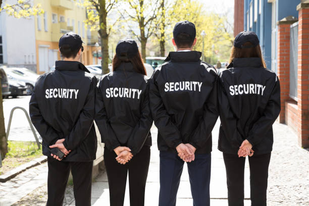 Rear View Of Security Guards With Hands Behind Back Standing In A Row